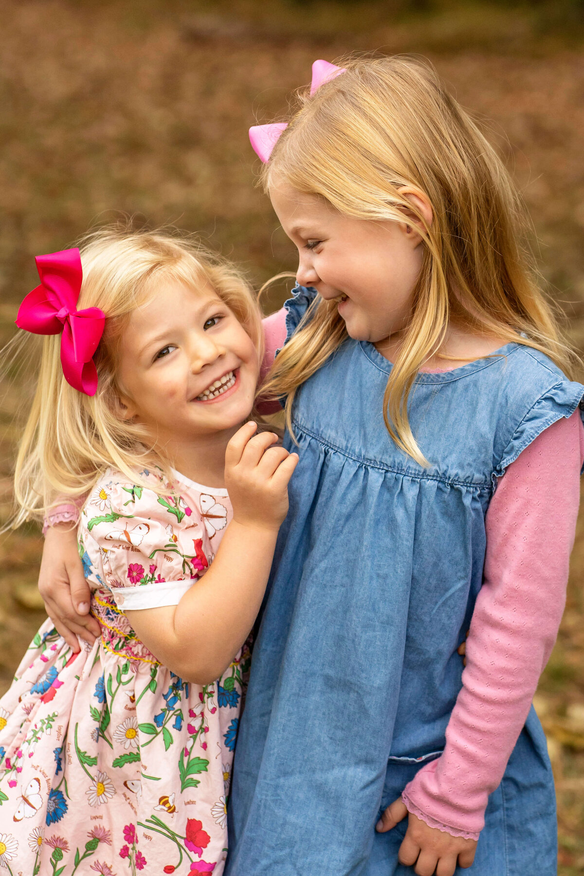 Two young sisters laughing together with brown leaves in background