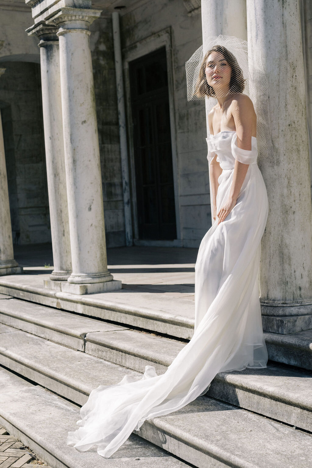 bride in wedding dress leaning against mansion columns