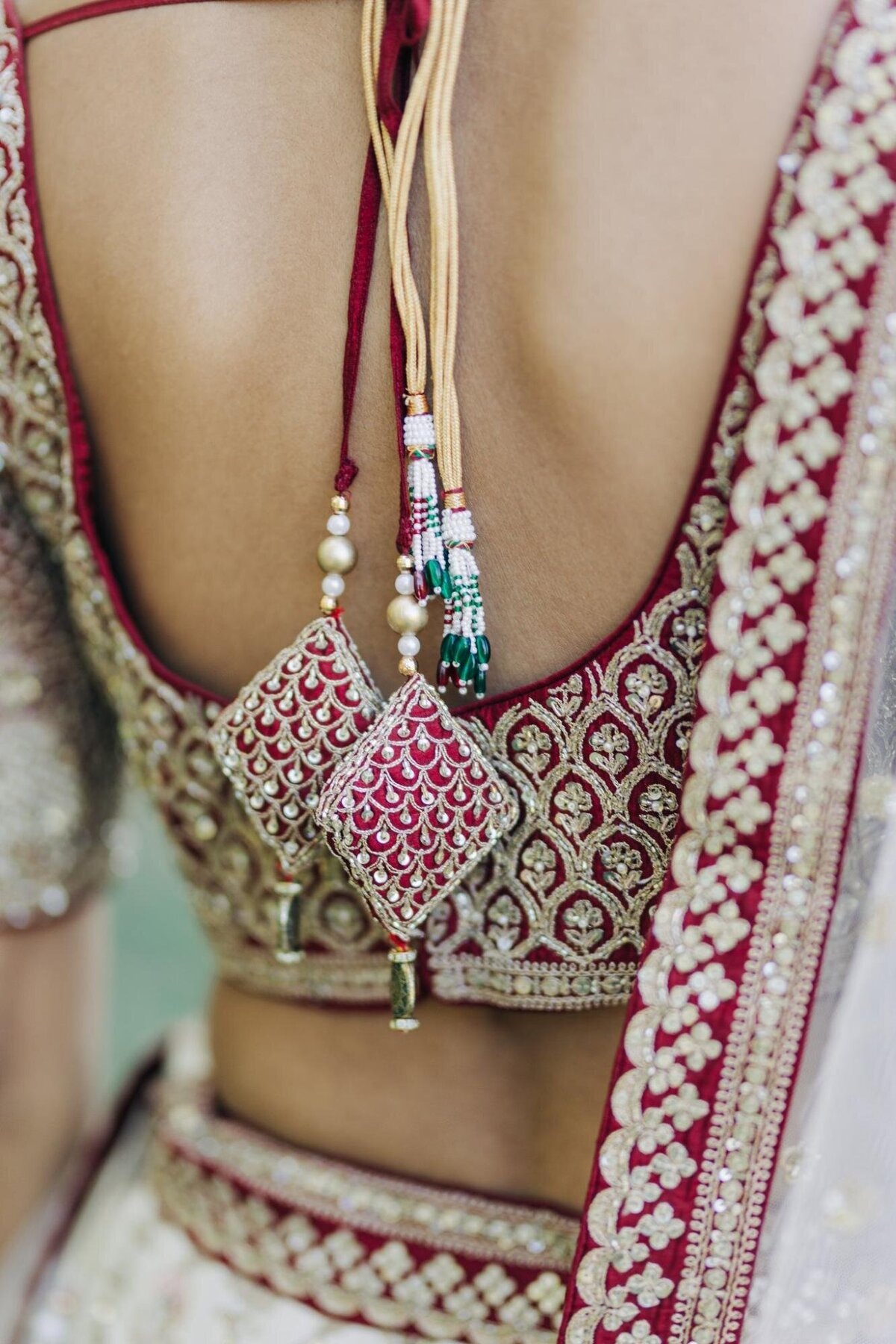 Close-up of a woman in a traditional embroidered red and white saree, focusing on the intricate patterns and beadwork on the blouse and saree border.