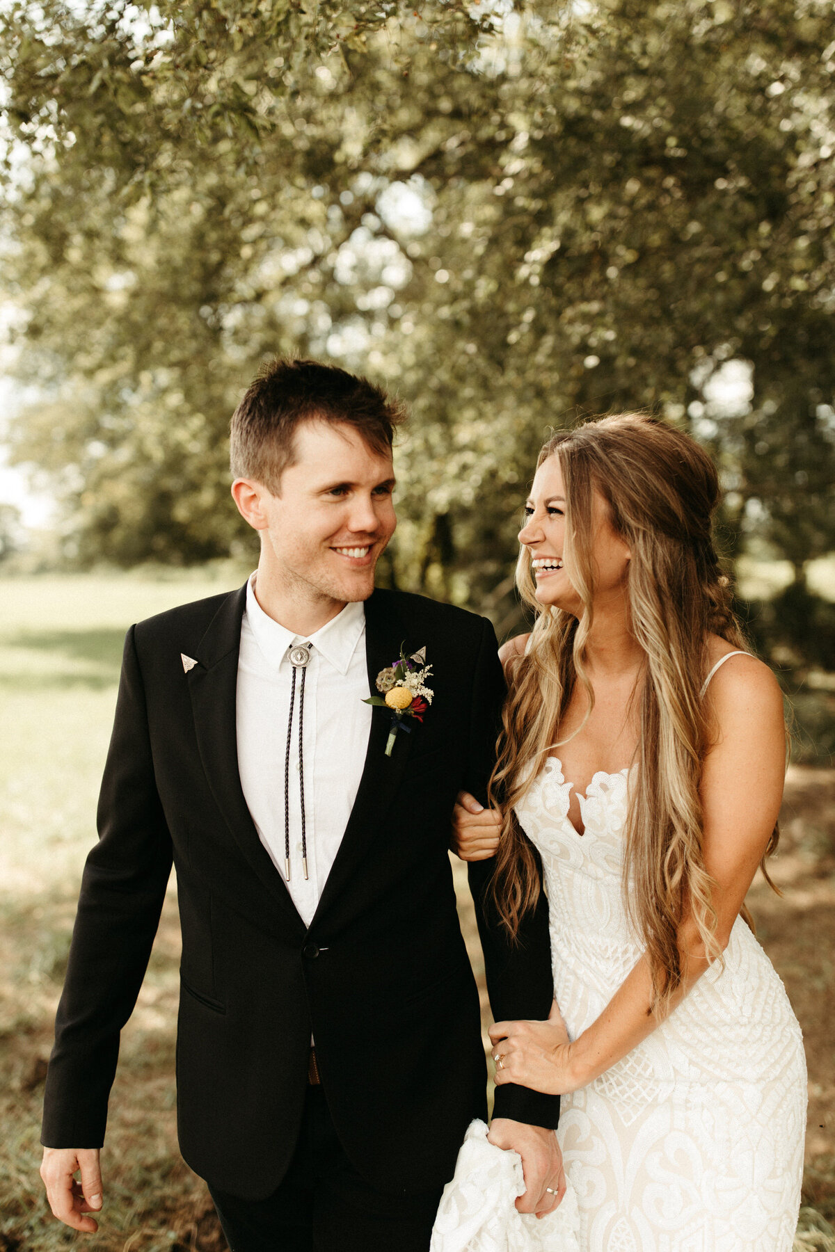 Bride holding groom's arm and looking at him while they laugh and walk together