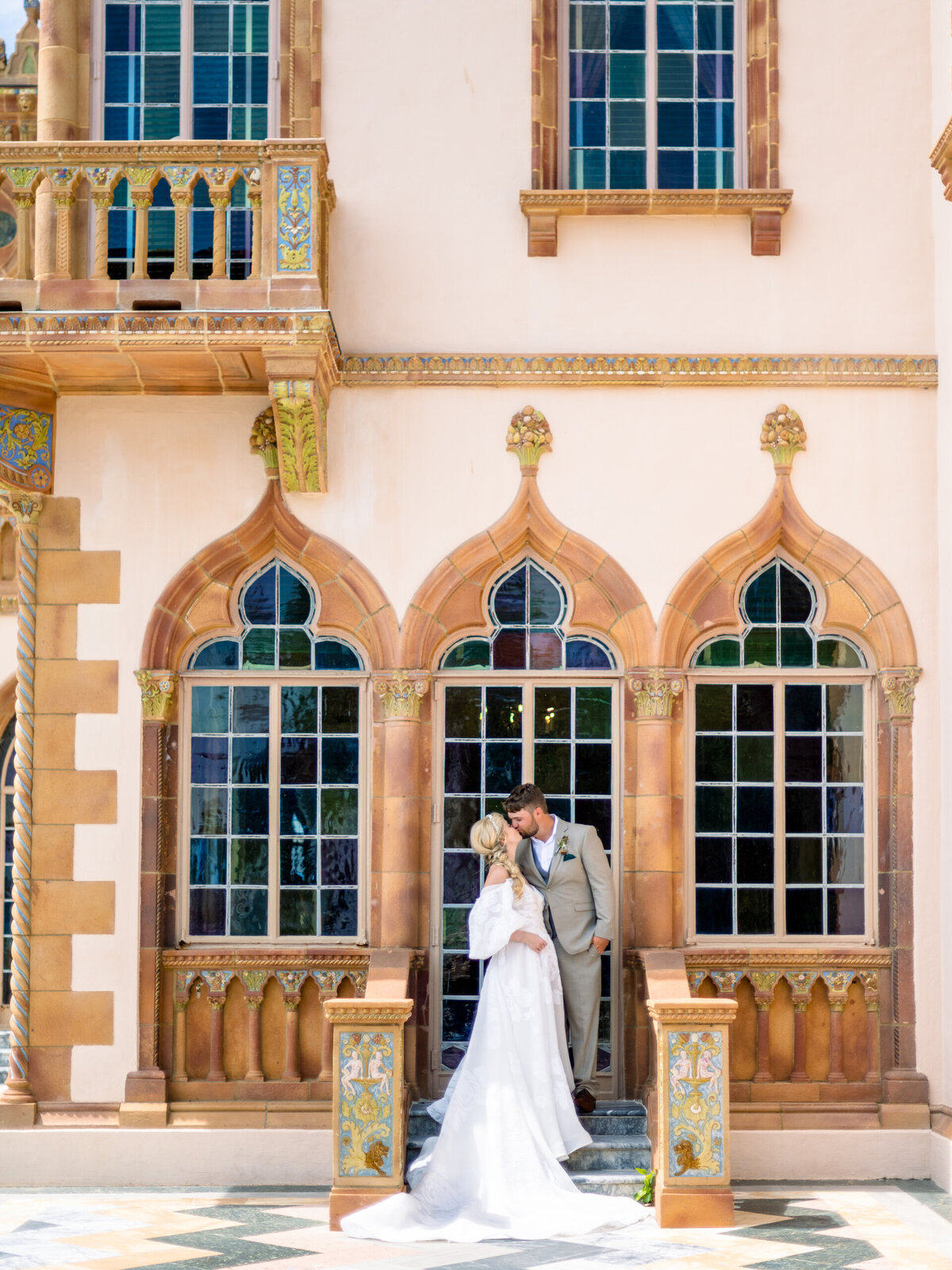 bride and groom kissing in front of an arched window