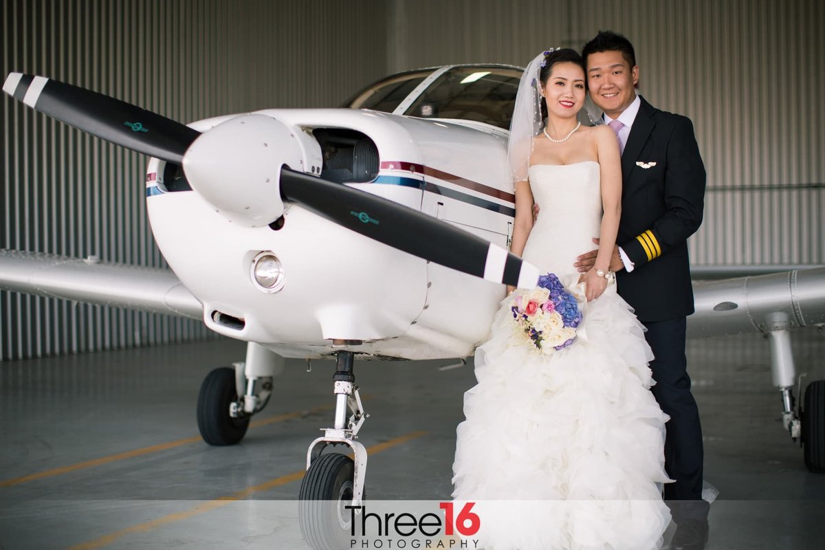 Newly married couple pose in front of small airplane