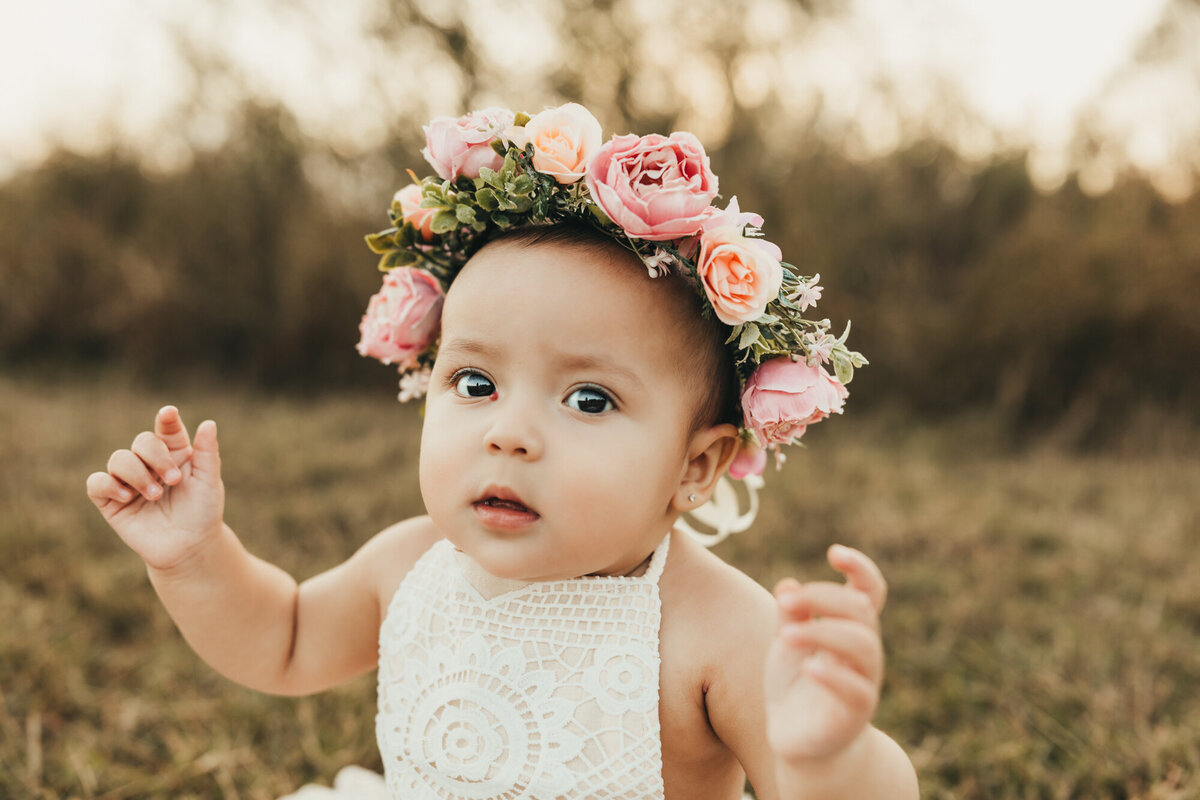 wearing a flower crown, little girl smirks at camera.