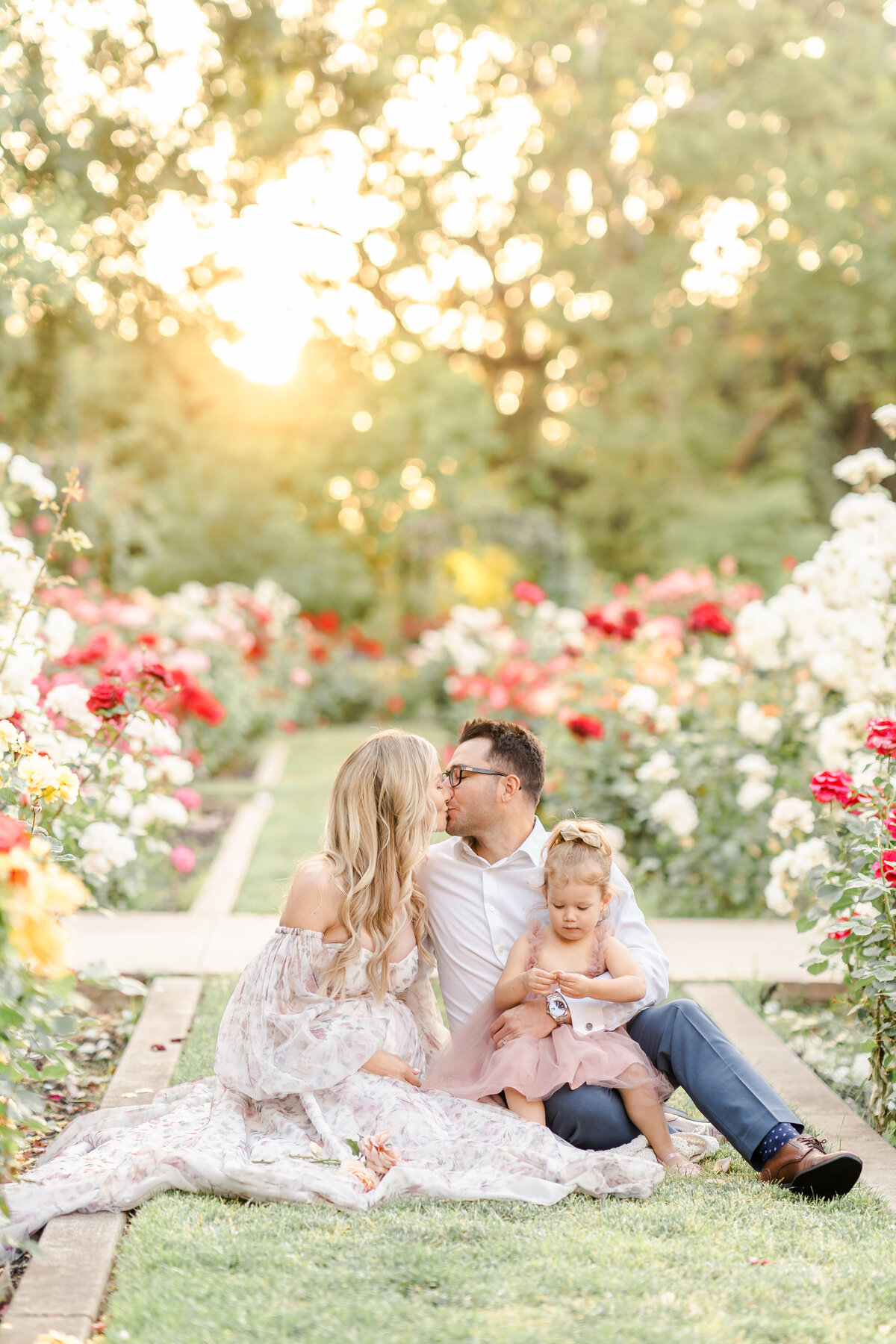 A family sits together in a rose garden while mom and dad share a kiss photographed by Bay area photographer, Light Livin Photography.