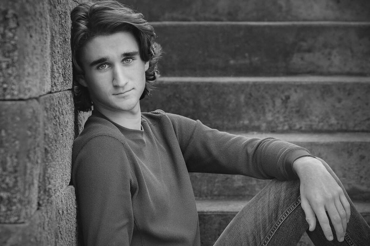 Black and white photograph of a HS senior looking straight at the camera while sitting on a concrete staircase.