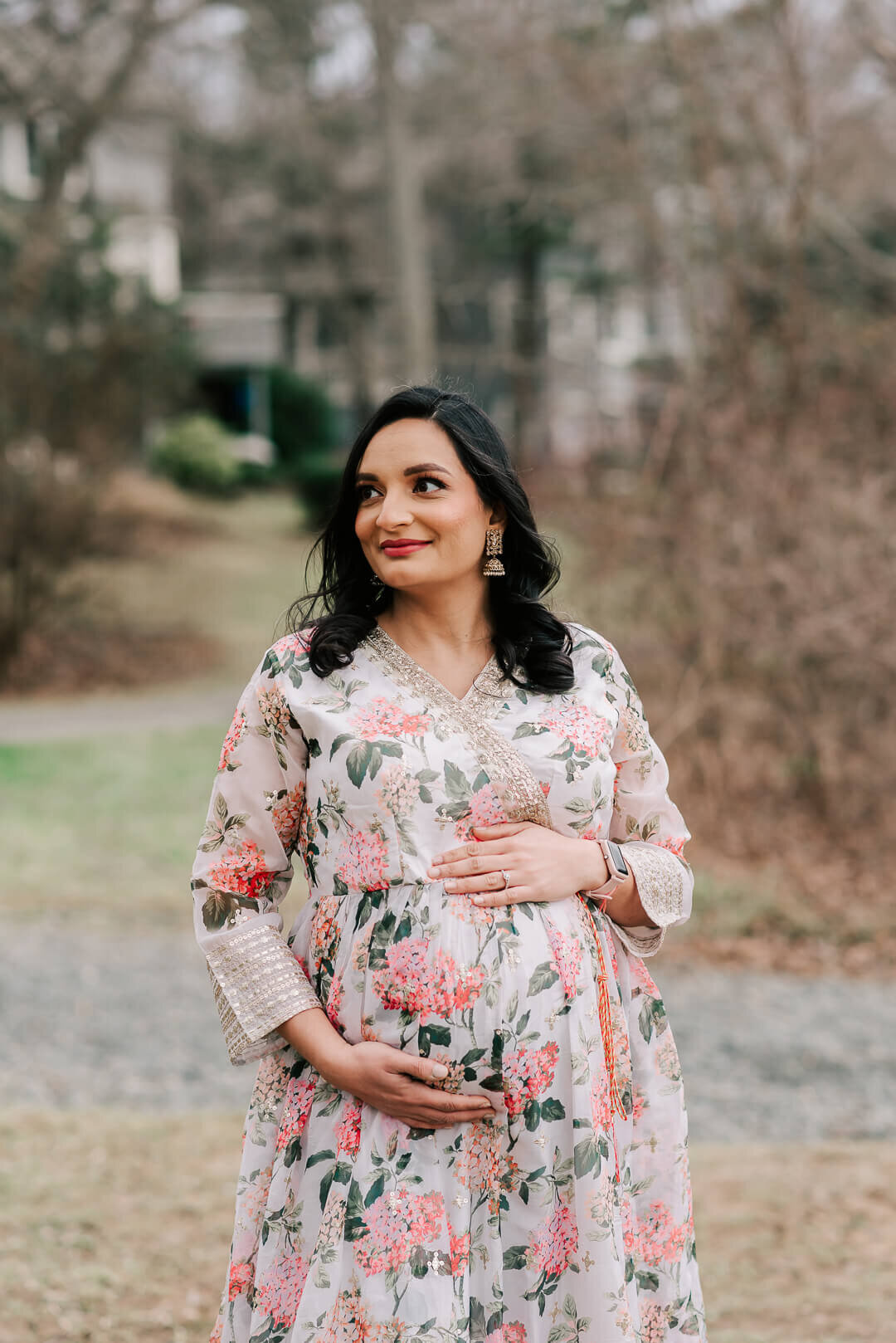 A pregnant Indian woman in a gorgeous floral dress, holding her belly at Lake Newport in Reston Virginia