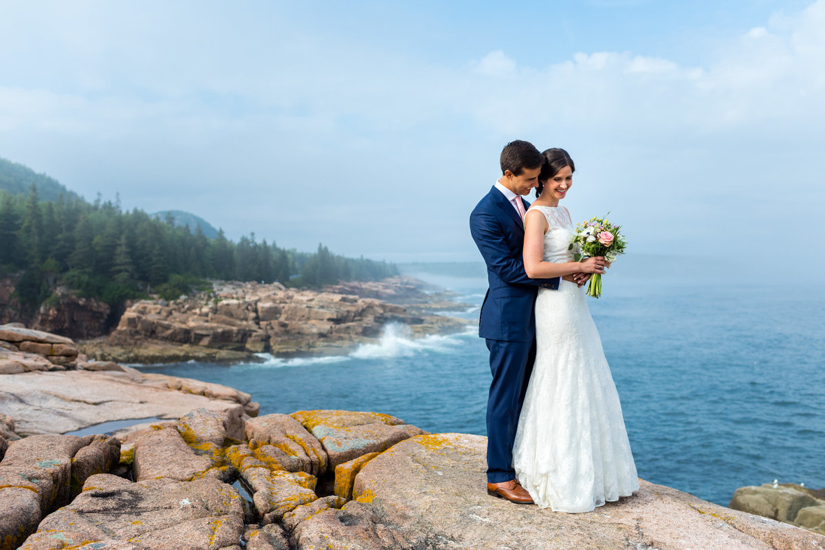 The bride and groom stand together on the cliffs of Acadia National Park after their Maine elopement