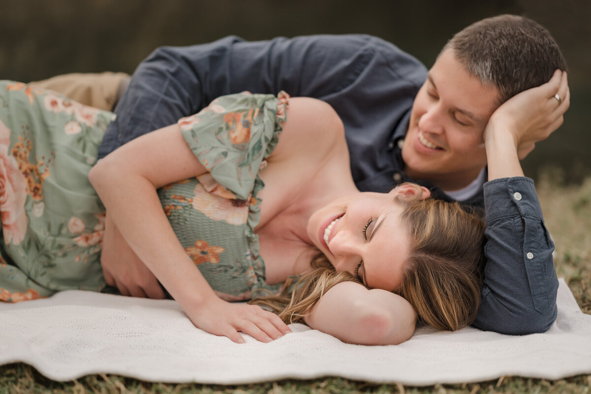 Portrait of a man and woman on a blanket in a park. She's smiling and his arm is around her.