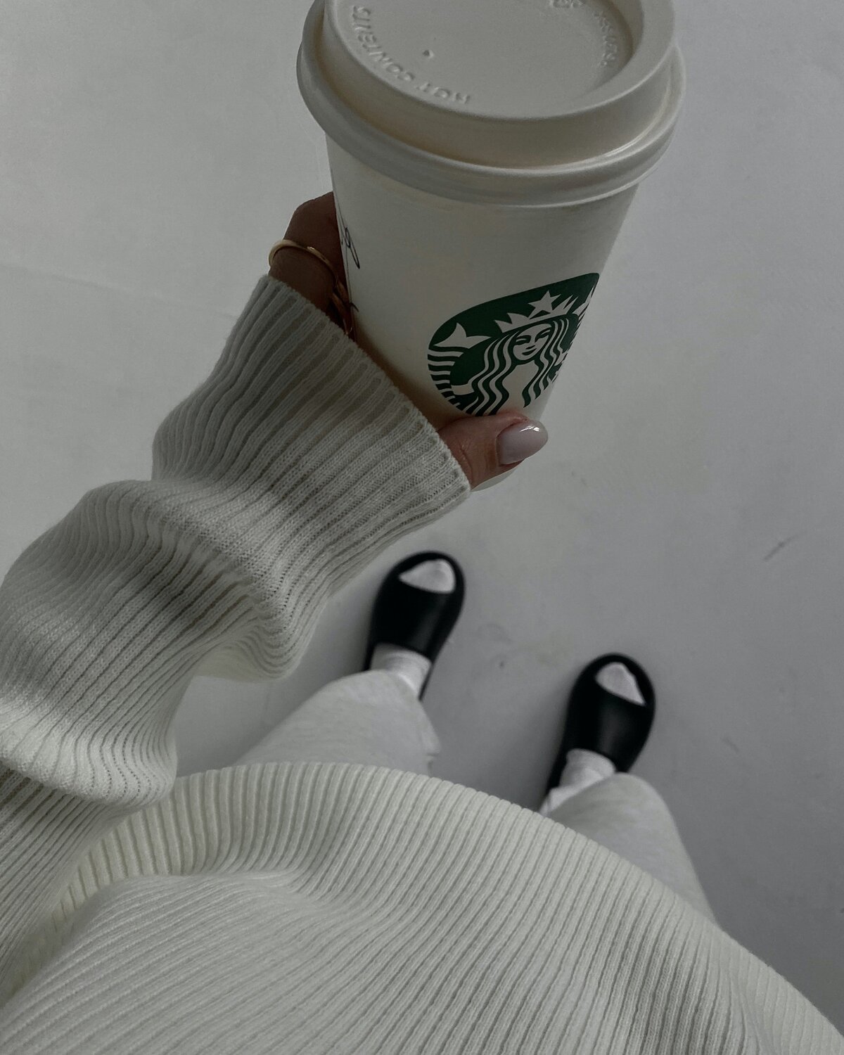 Woman in white with black sliders holding starbucks coffee