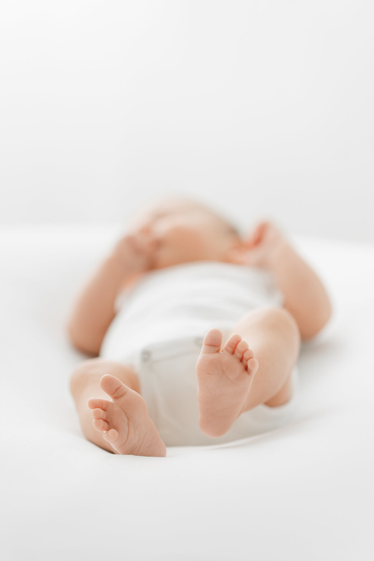 A DC newborn photography photo of a baby laying on its back on a white blanket in front of a window focused on its feet