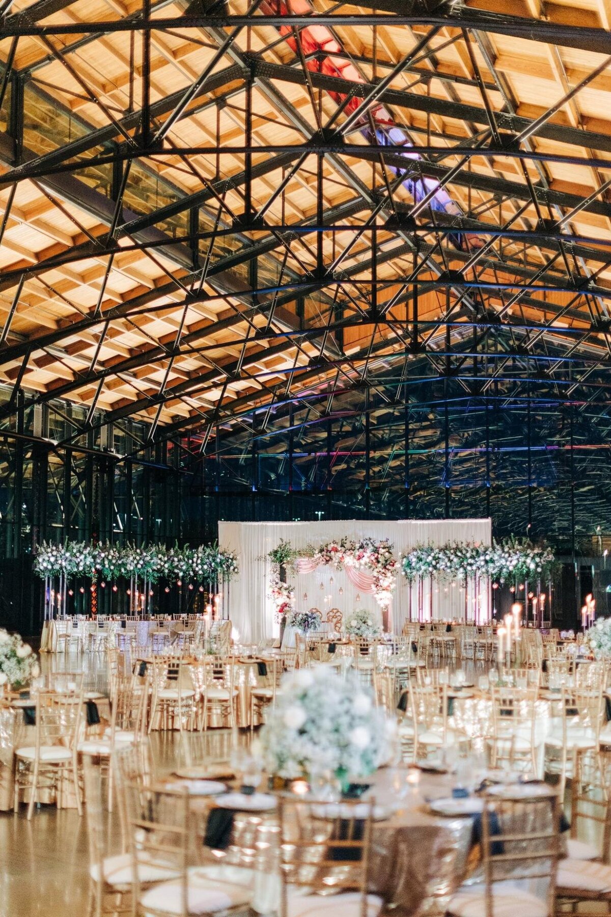 Elegant wedding reception inside a glasshouse with floral decorations and round tables set for dining.