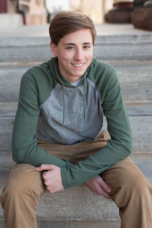 Senior boy in gray and green shirt sitting on granite step, smiling at camera