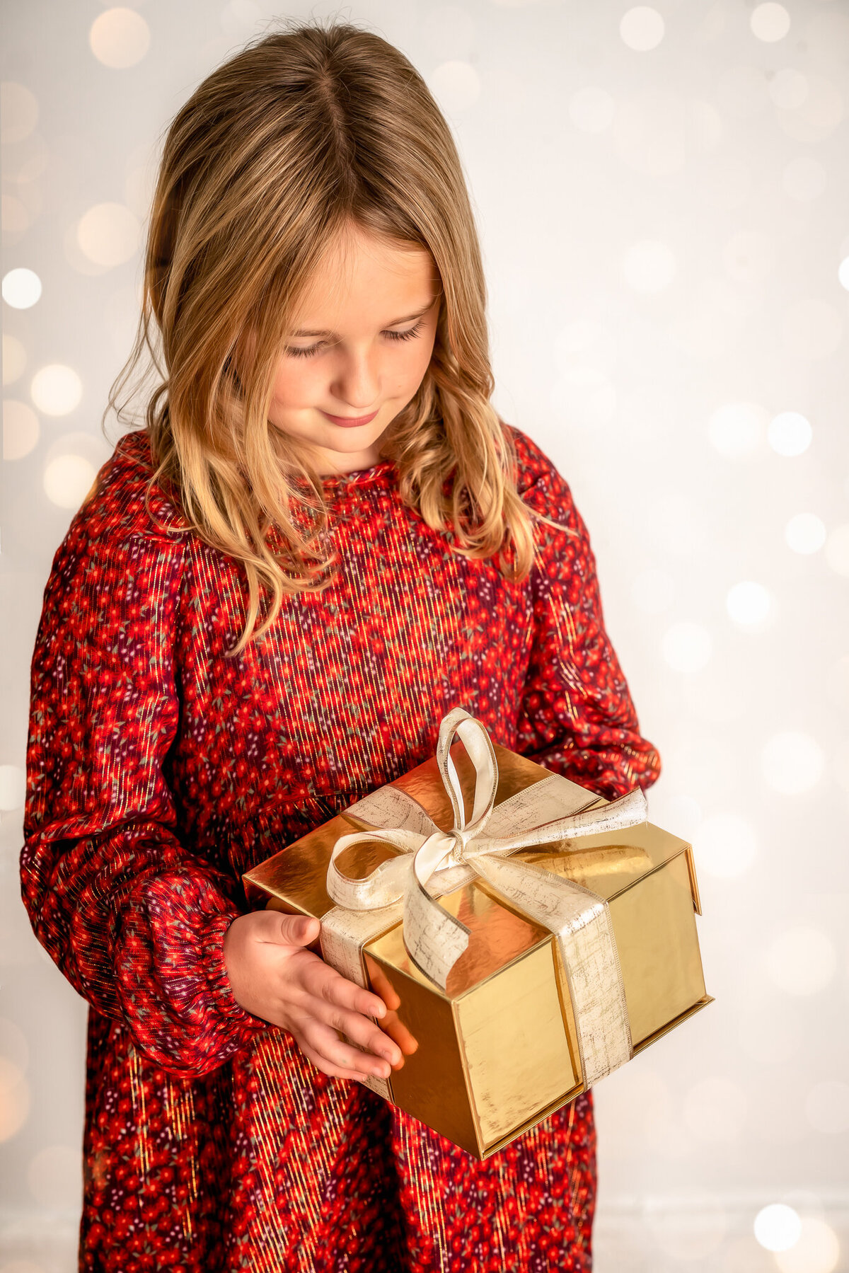 A young child is looking down at a Christmas present with a large gold ribbon.