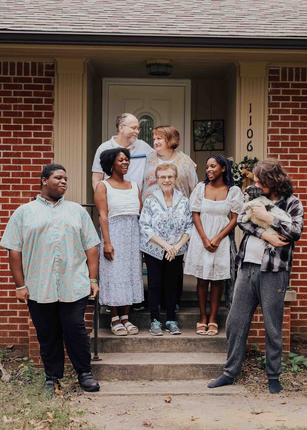 Maddie Rae Photography family photo, grandma, mom and dad, and four kids standing on the front steps all looking at each other smiling
