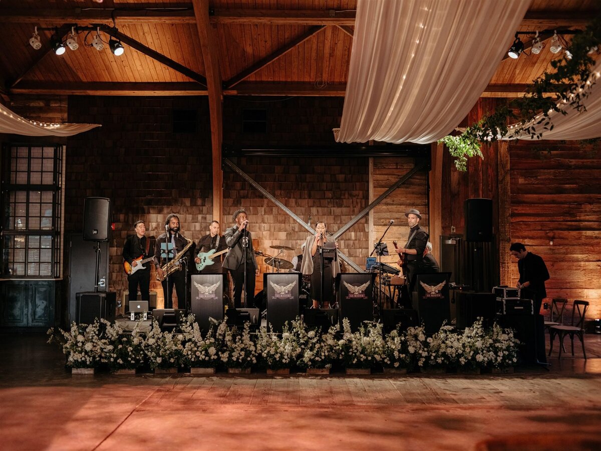 Cedar Lakes Estate wedding venue reception space with large wood dance floor, live band surrounded by white florals, and an elegant white fabric swag.