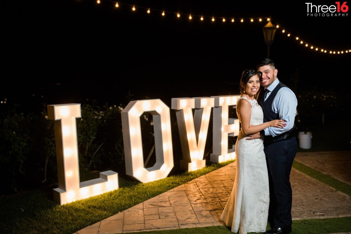 Bride and Groom  pose on the dance floor in front of the Love sign