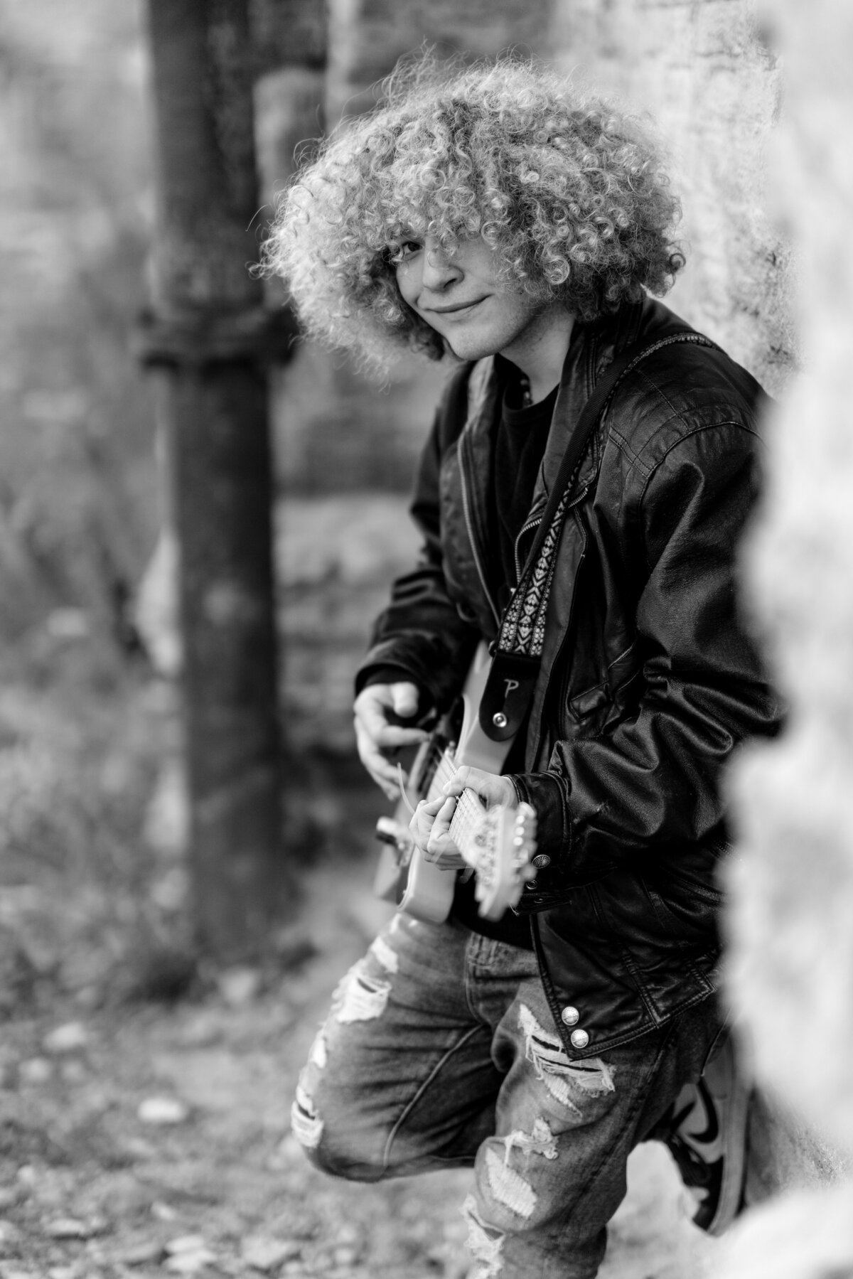 Senior boy with afro dressed in leather jacket plays guitar.