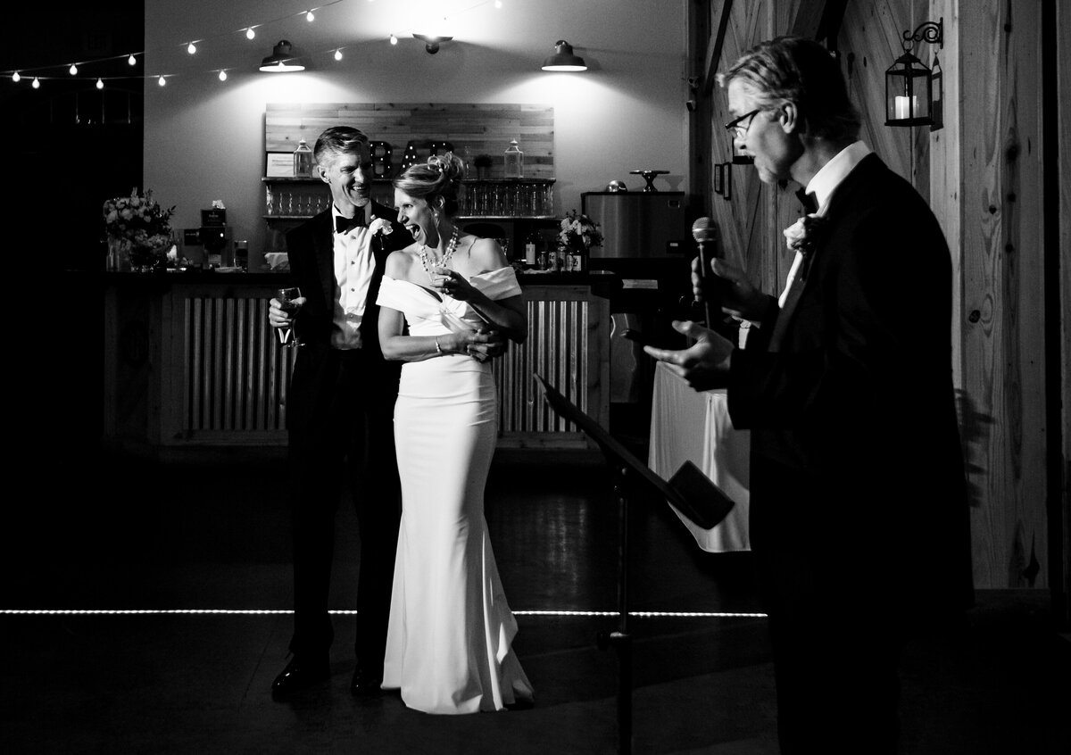 Black-and-white-image-of-a-couple-laughing-and-reacting-to-best-man-giving-speech-in-the-foreground-at-Alexander-Homestead