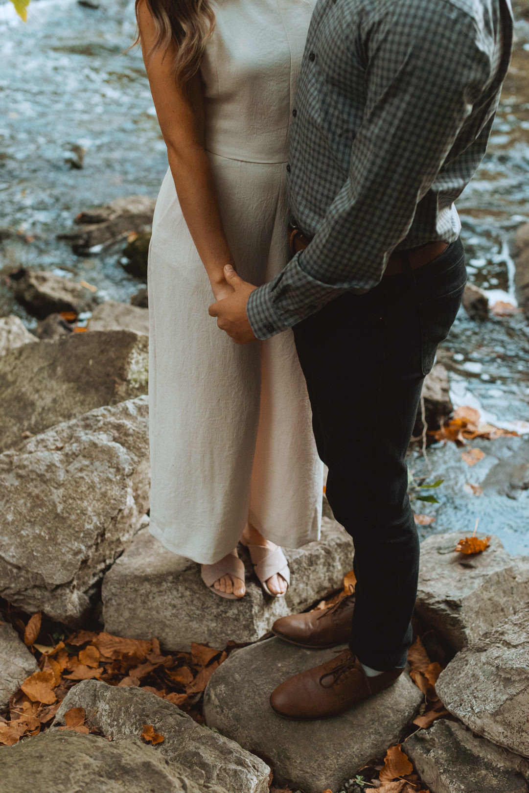 engaged couple standing on the rocks by the river