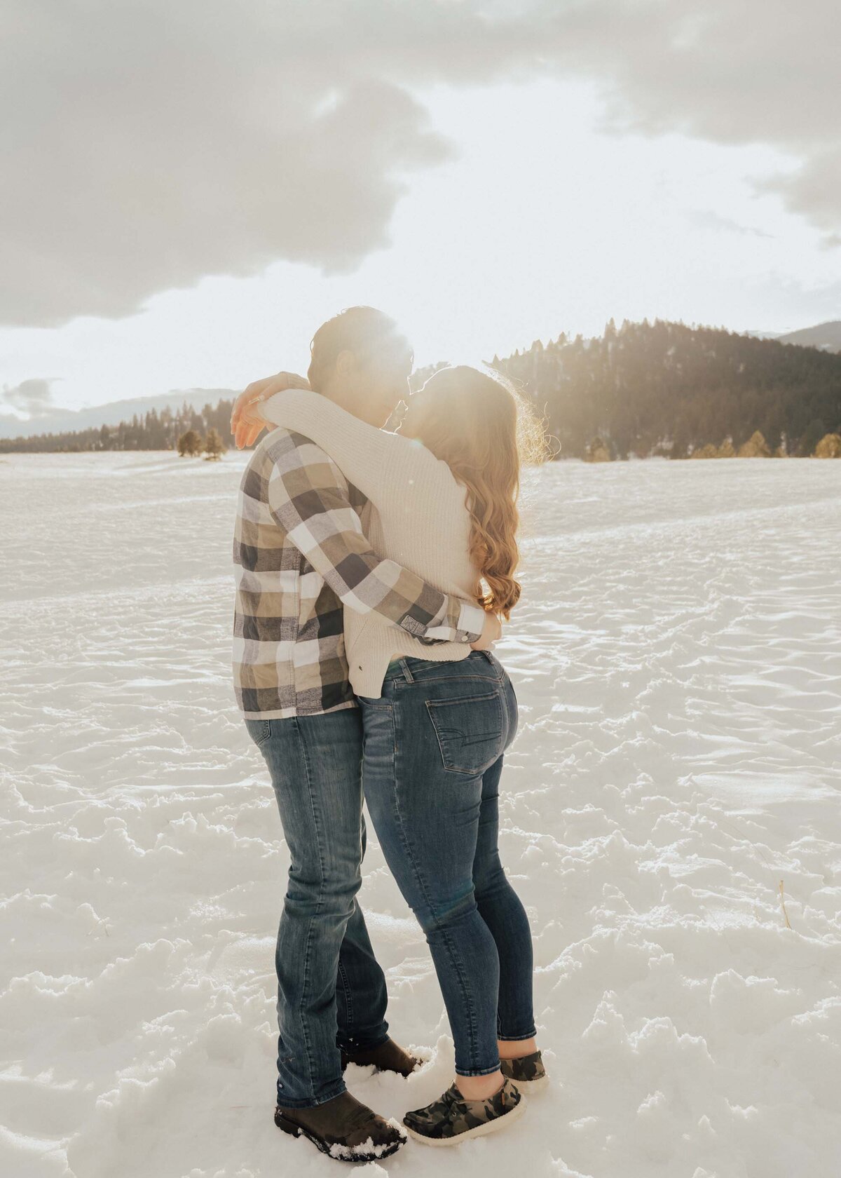 Maddie Rae Photography couple standing face to face giving eskimo kisses. there are mountains and snow in the background. the sun is shining through