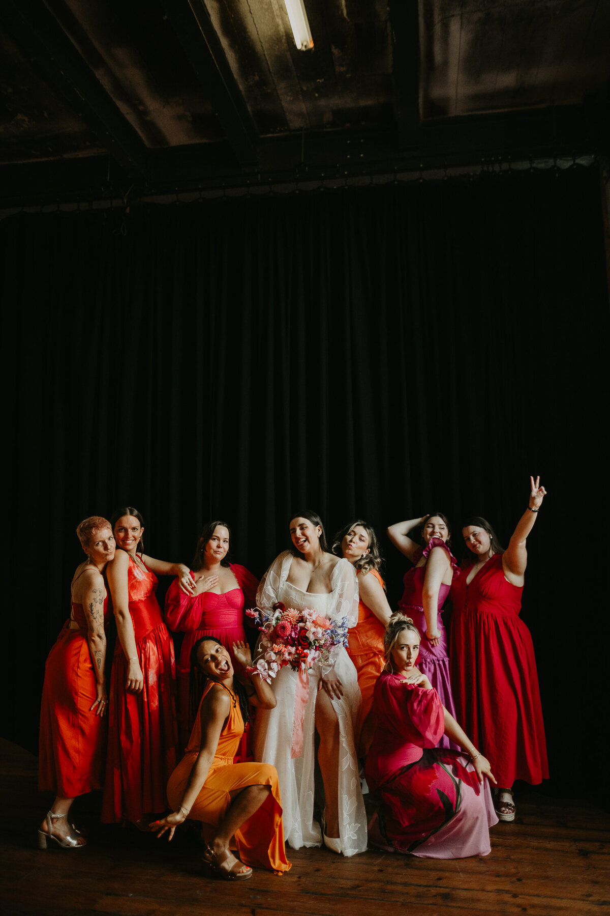 A bride and her wedding party who are all wearing orange and pink bridesmaids dresses at Paintworks in Bristol. 