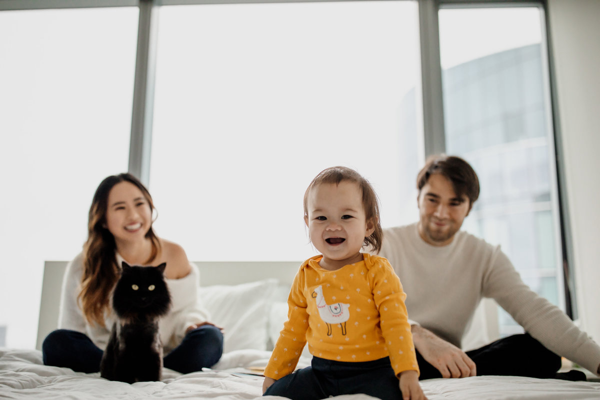 San Francisco in home family photography session with toddler laughing on bed with parents and cat