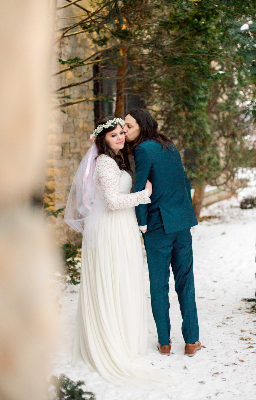 plummer house elopement winter in rochester minnesota bride and groom walk together beside winona stone building and pine trees