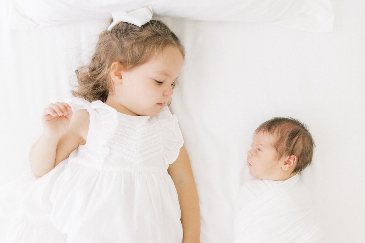 2 year old little girl looking at her newborn baby brother during their newborn photo session
