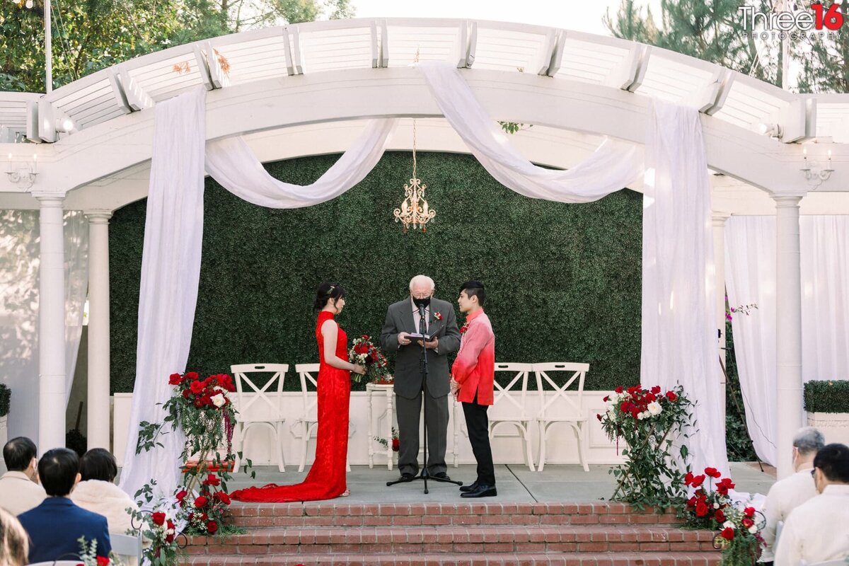 Bride and Groom dressed in red face each other during their wedding ceremony at the Noriega House in Bakersfield, CA