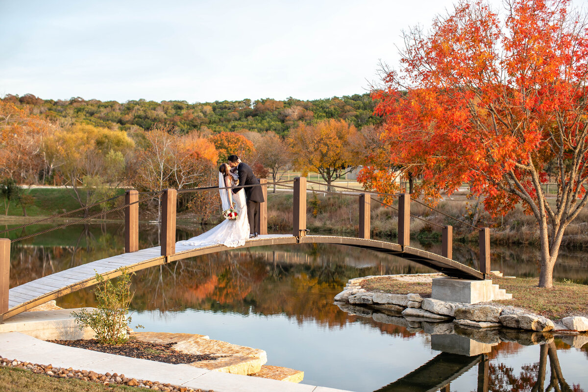 bride and groom kiss on bridge at fall wedding Sendera Springs Kerrville Texas  by Firefly Photography