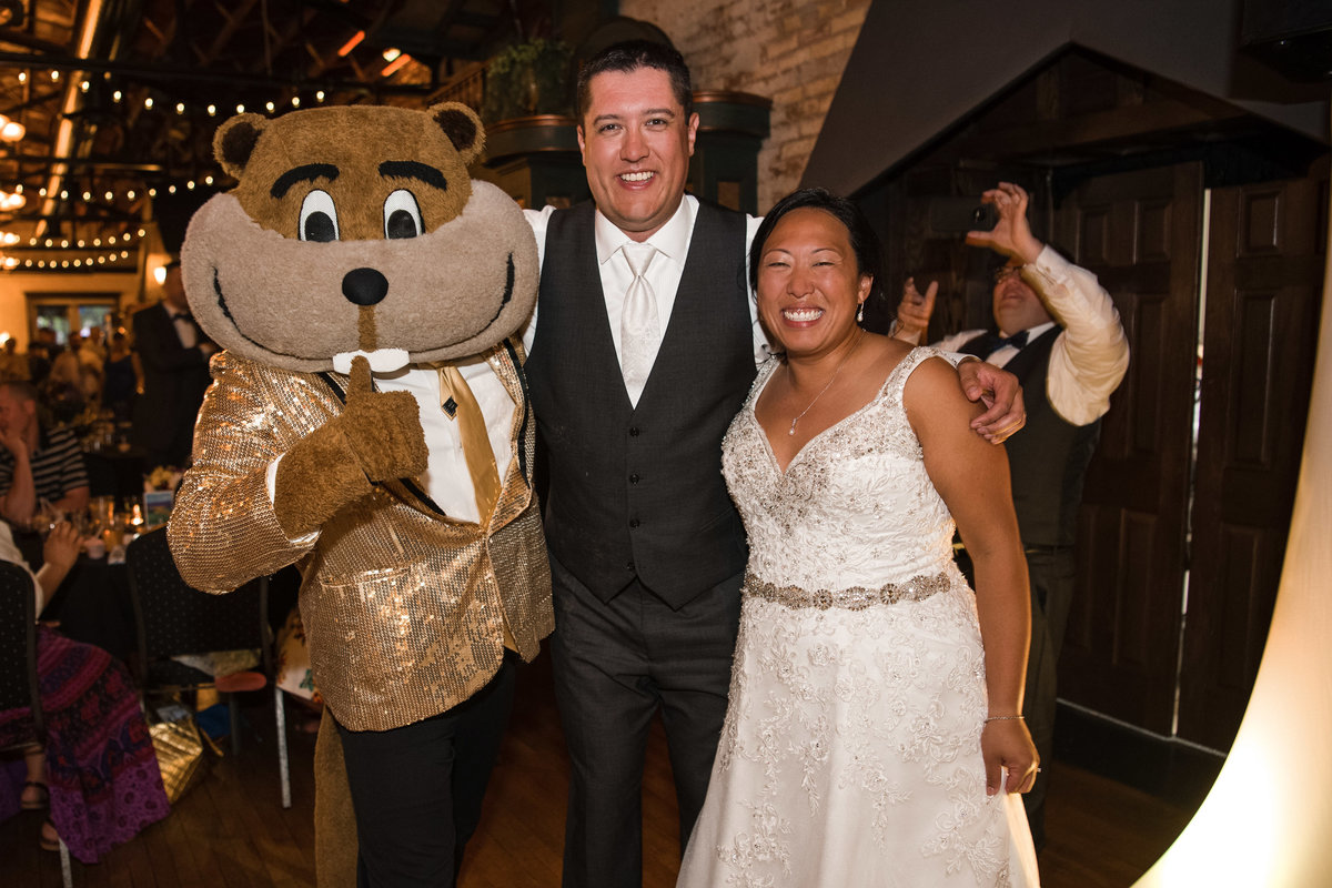 Bride and groom smile with Goldy Gopher at reception.