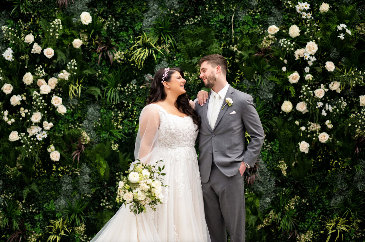 A bride and groom standing in front of the ivy wall inside the atrium at Perona Farms
