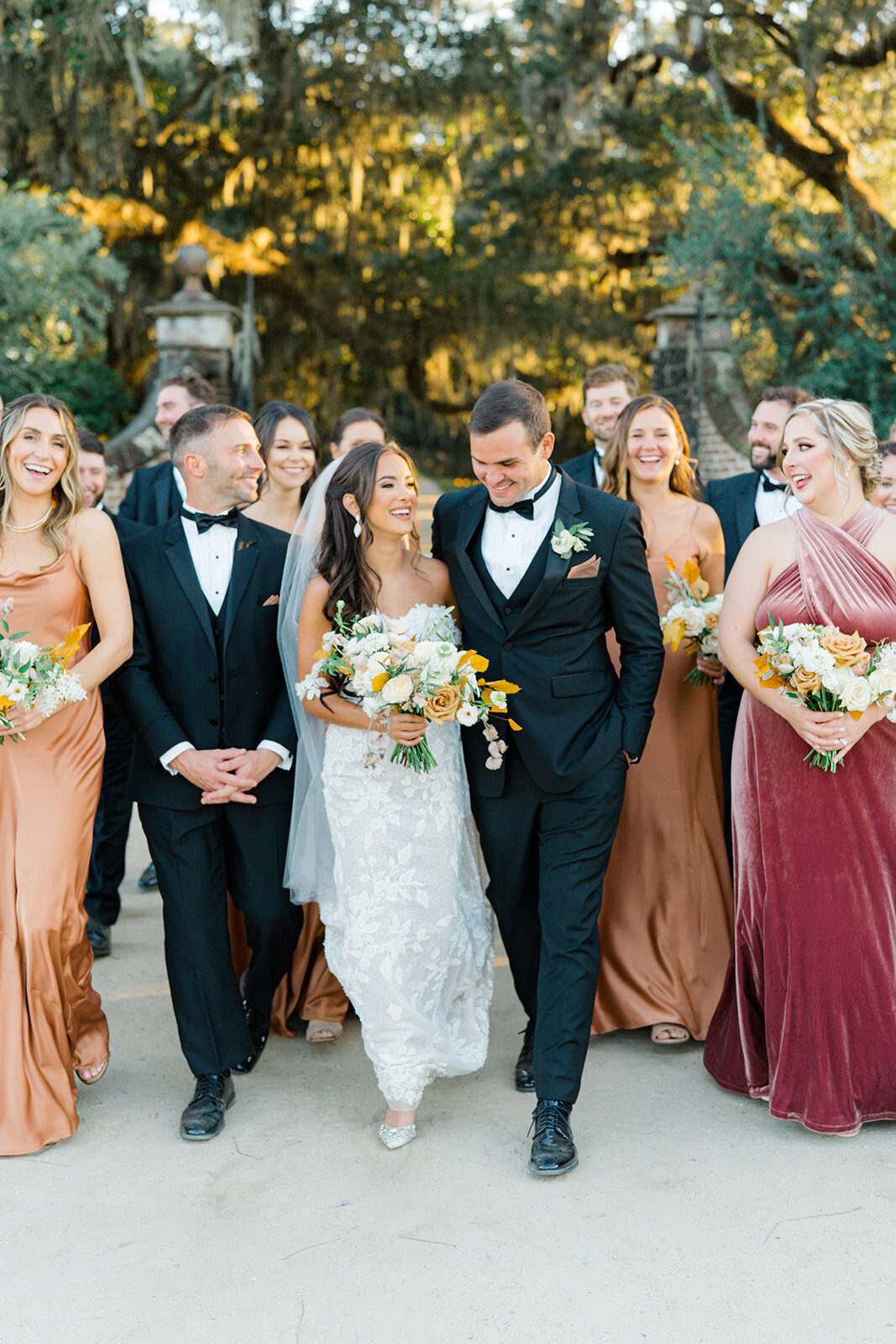 Boone Hall Fall Wedding. Golden sunset light hitting spanish moss and live oak trees. Bridesmaids in jewel-toned dresses. Full bridal party walking with bride and groom. Charleston destination wedding photographer.