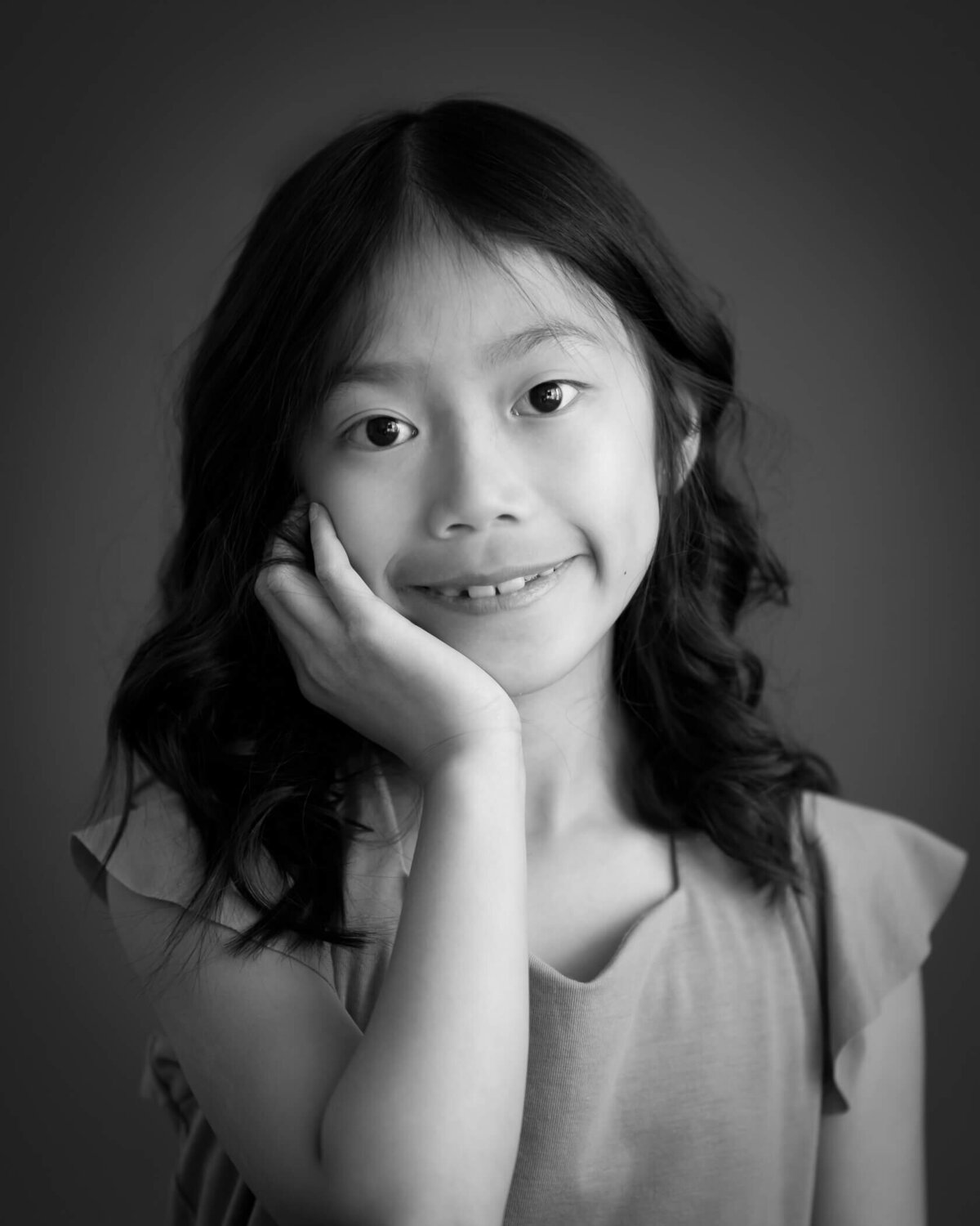 black & white photo of 10 year old girl resting face on hand and smiling