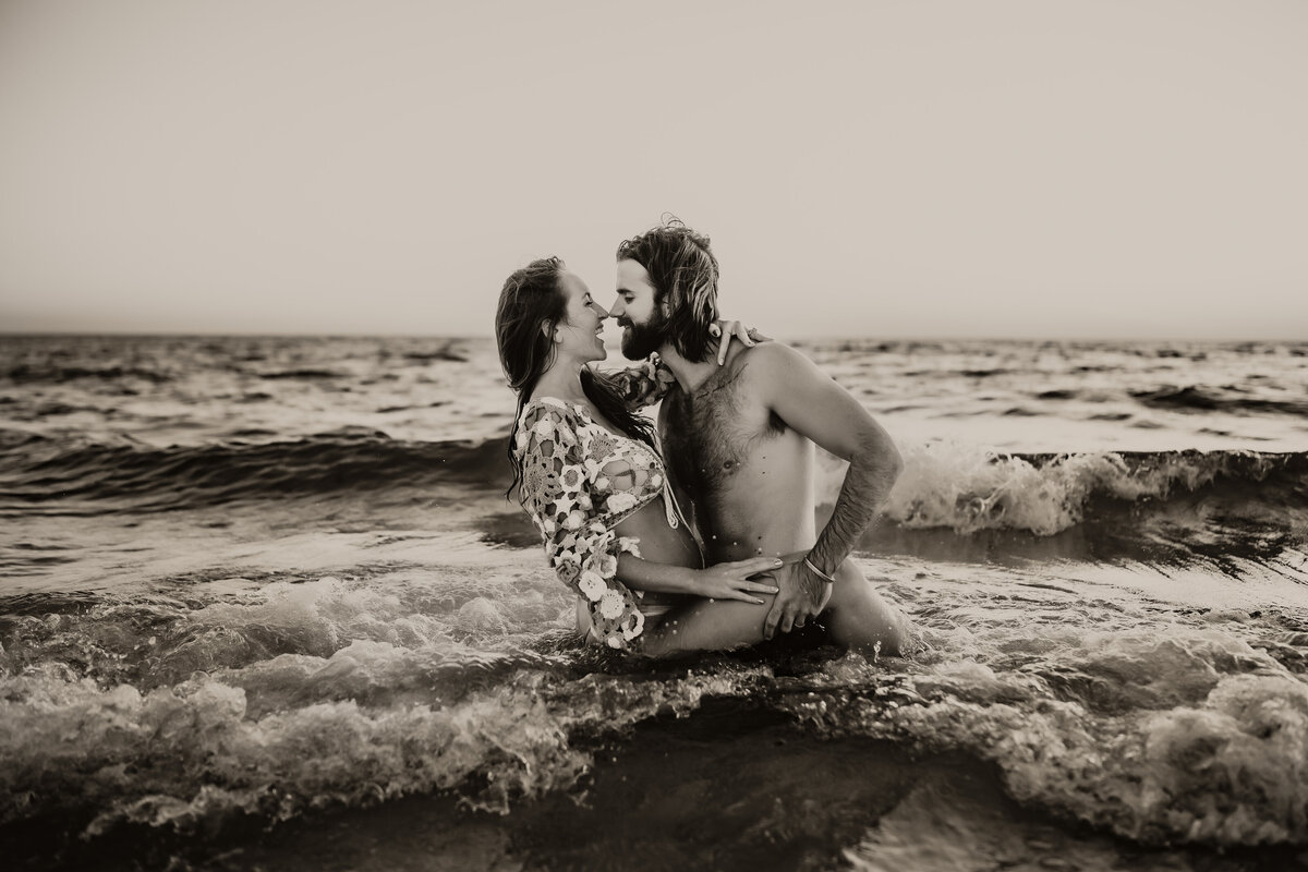 sexy, fun couples beach photo shoot in black and white with a couple sitting in the water at sundown