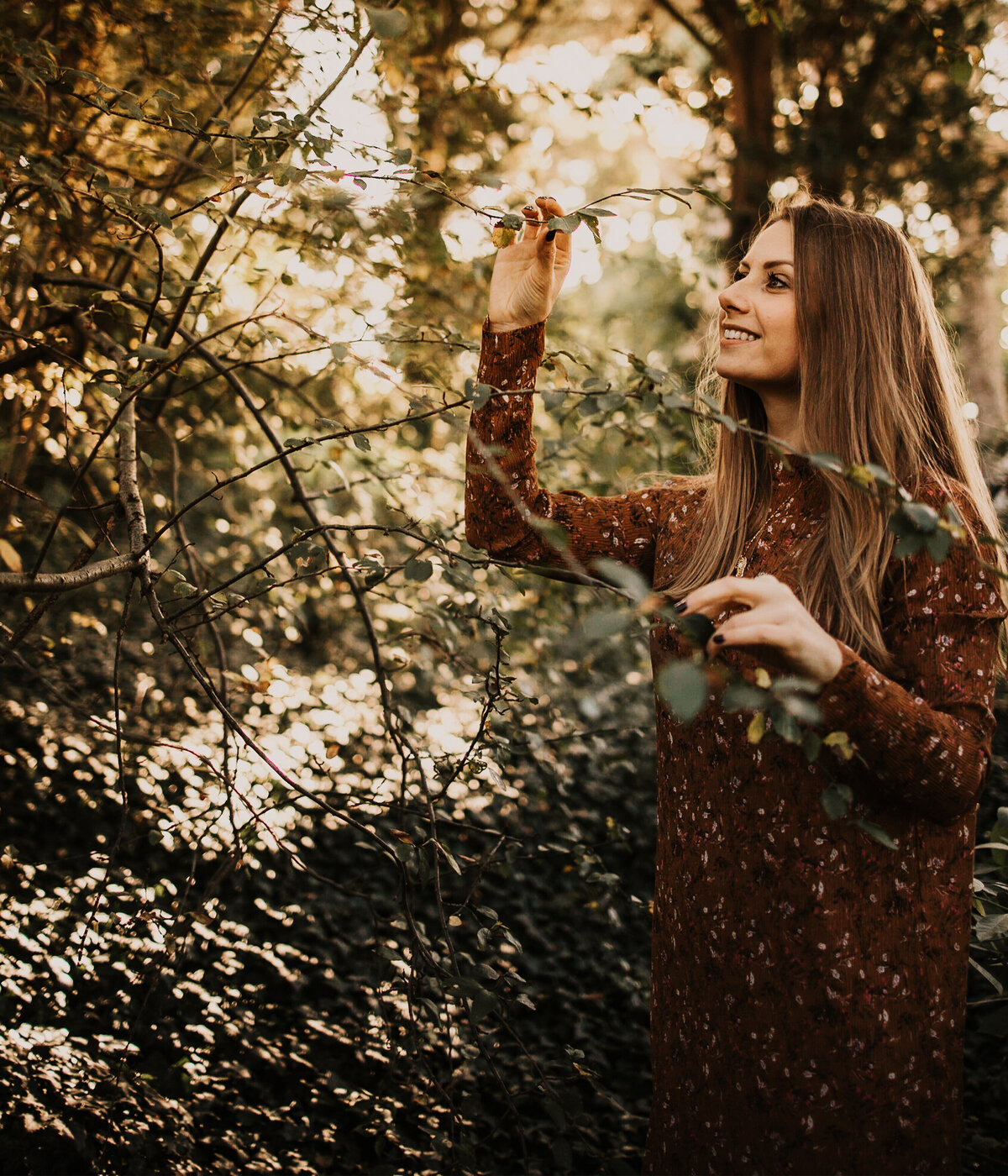 Barbora is surrounded by trees. She smiles and touches a branch