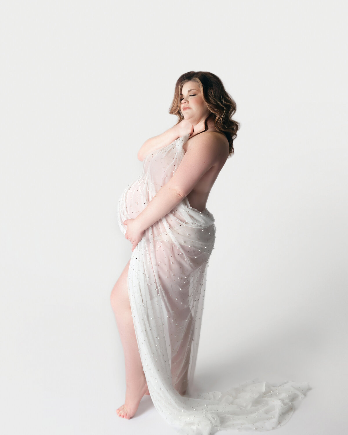 Pregnant women with white fabric draped over body during maternity photoshoot in Franklin Tennessee photography studio
