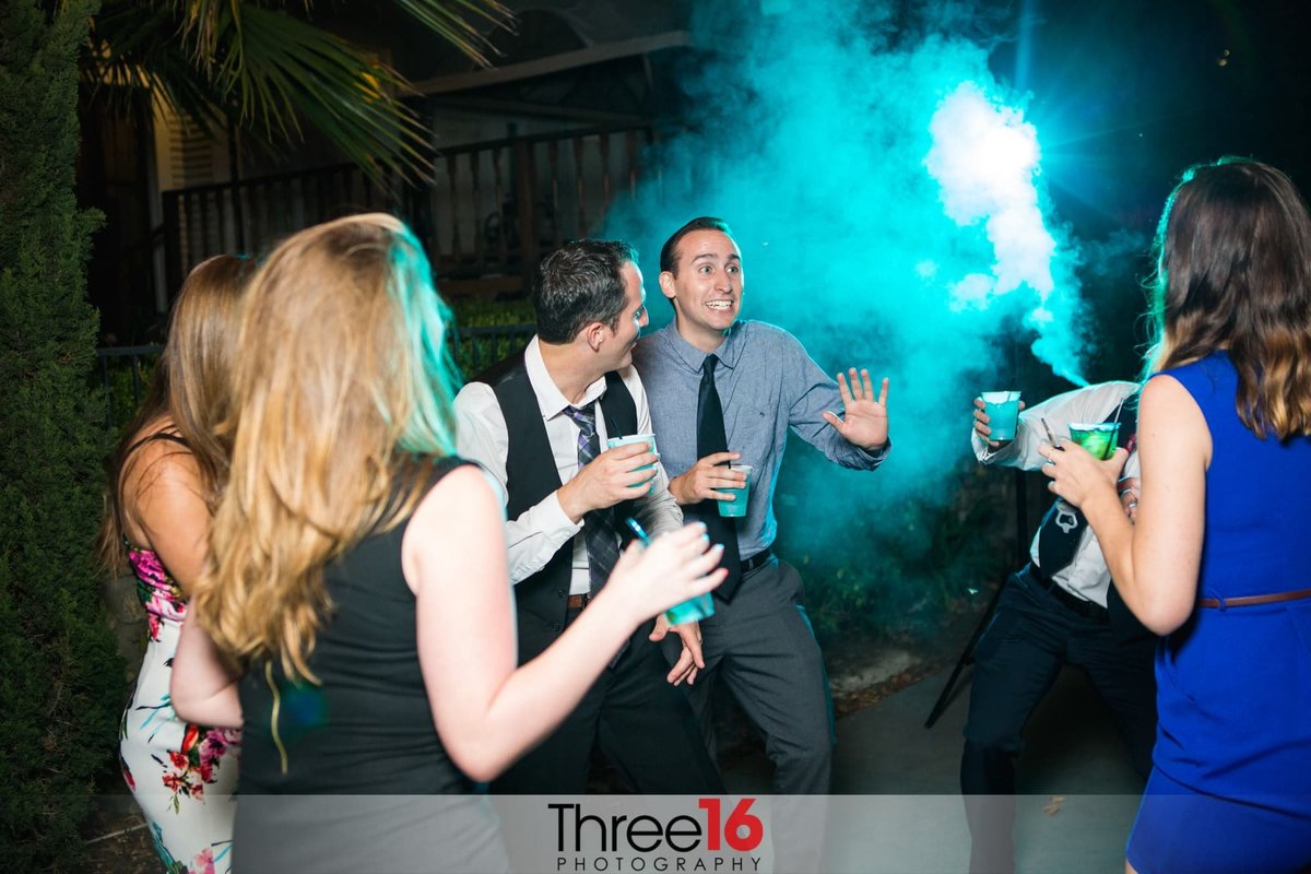 Guests interact during wedding reception at night with blue fog in the background