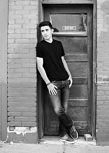 Black and white image High School senior guy leaning against old brick door opening .