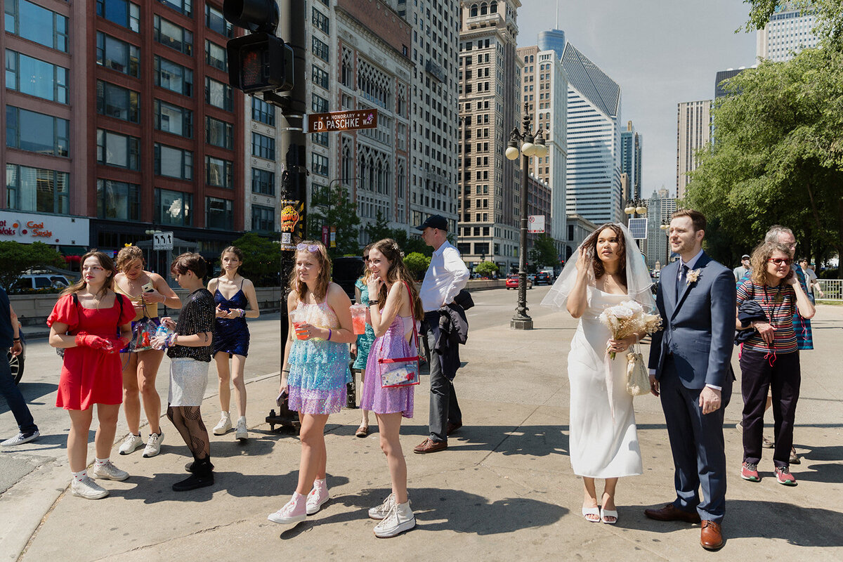 Just Married photo session couple stands on a Michigan Ave corner waiting to cross the street next to a group of Taylor Swift concert fans