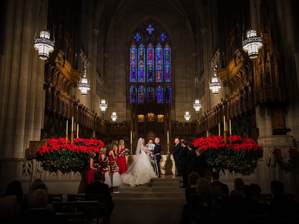 Bride and groom at the altar in the Duke Chapel decorated for Christmas, with the warm glow of candles and festive red poinsettias