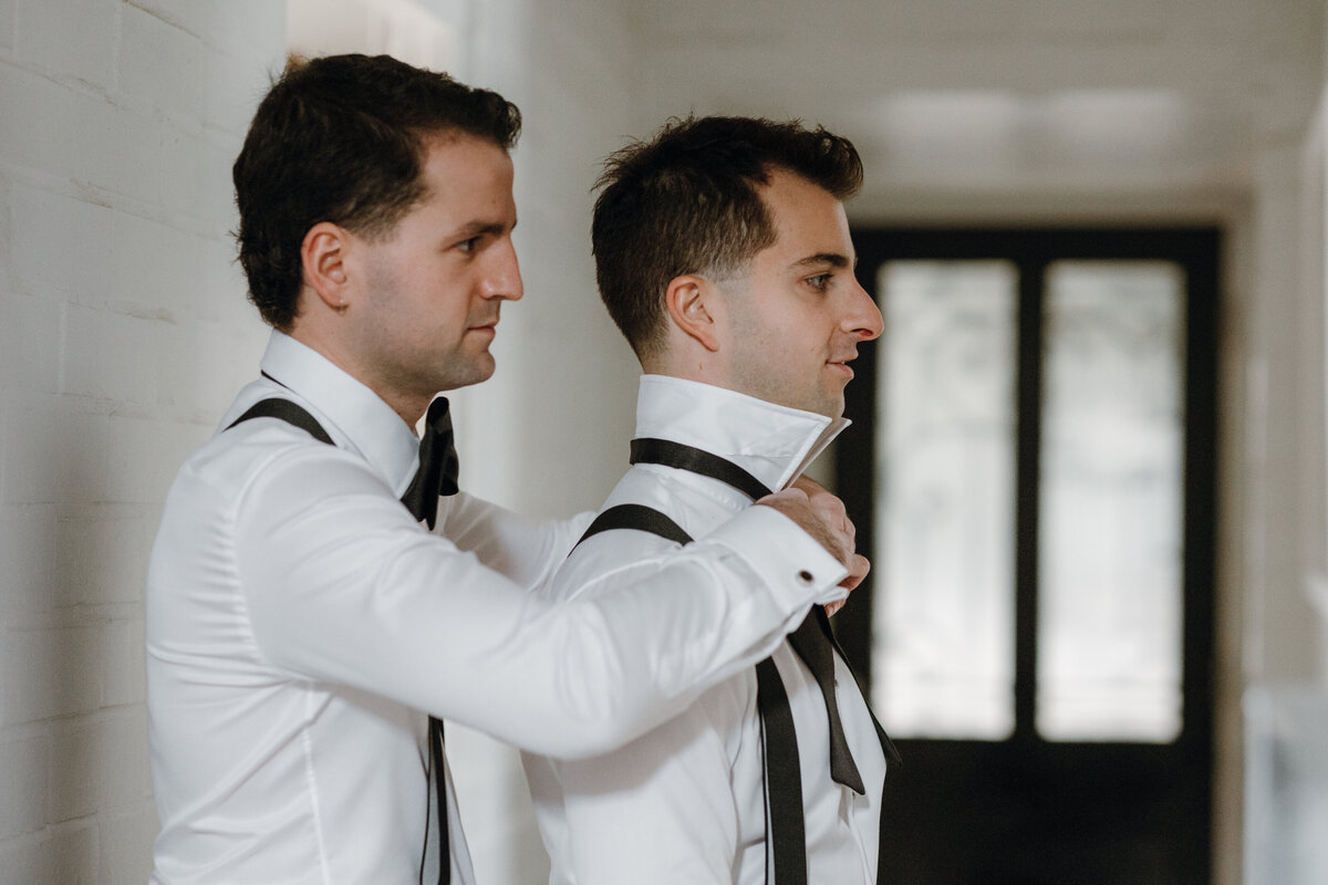 A groom putting on his groom's bow tie.
