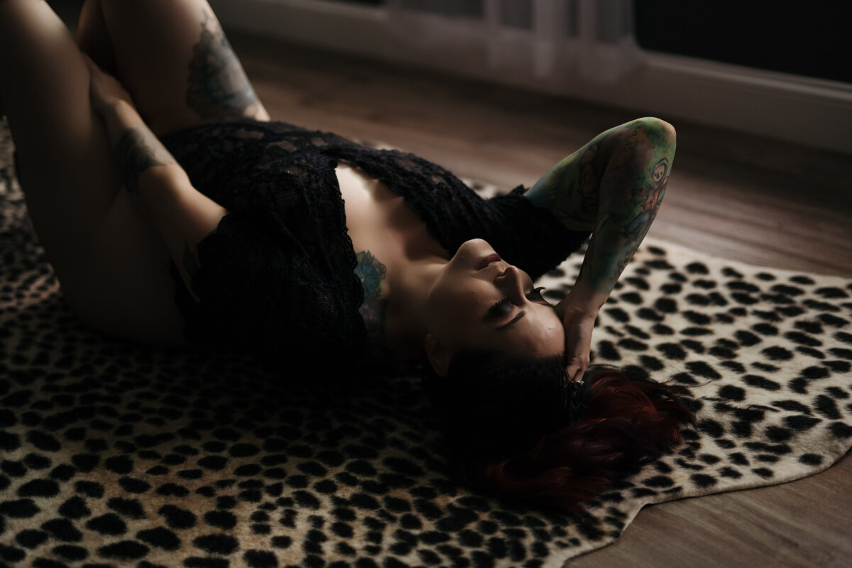 A woman in black lace lingerie lays on a cheetah print rug in a studio