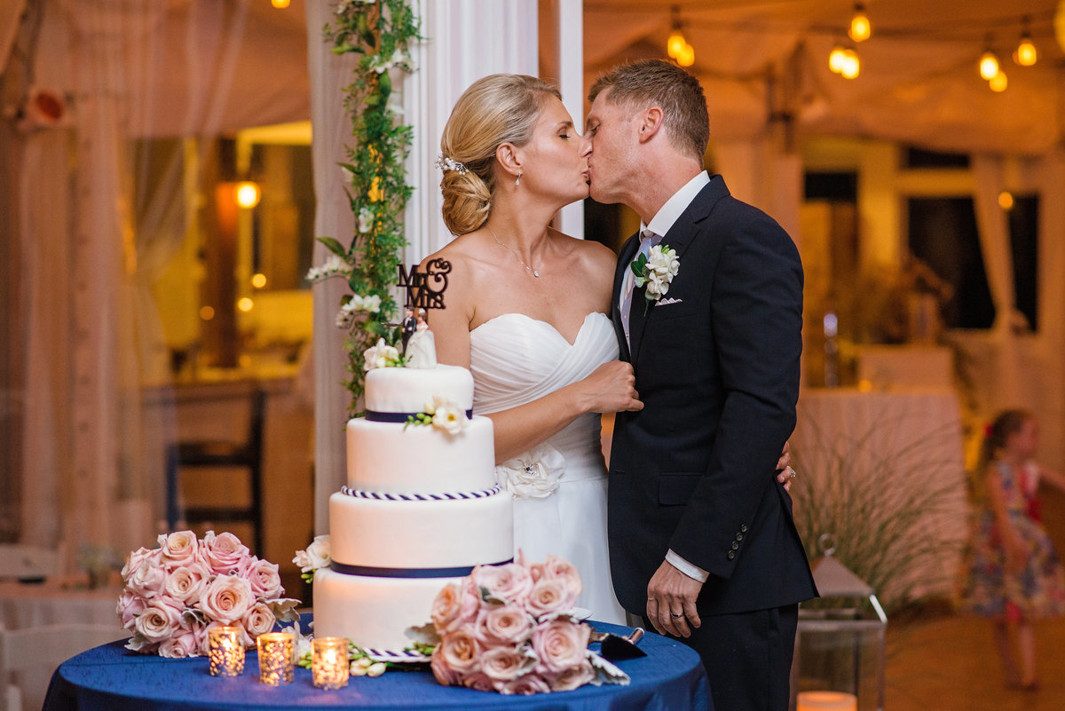 Bride and groom kissing next to the wedding cake