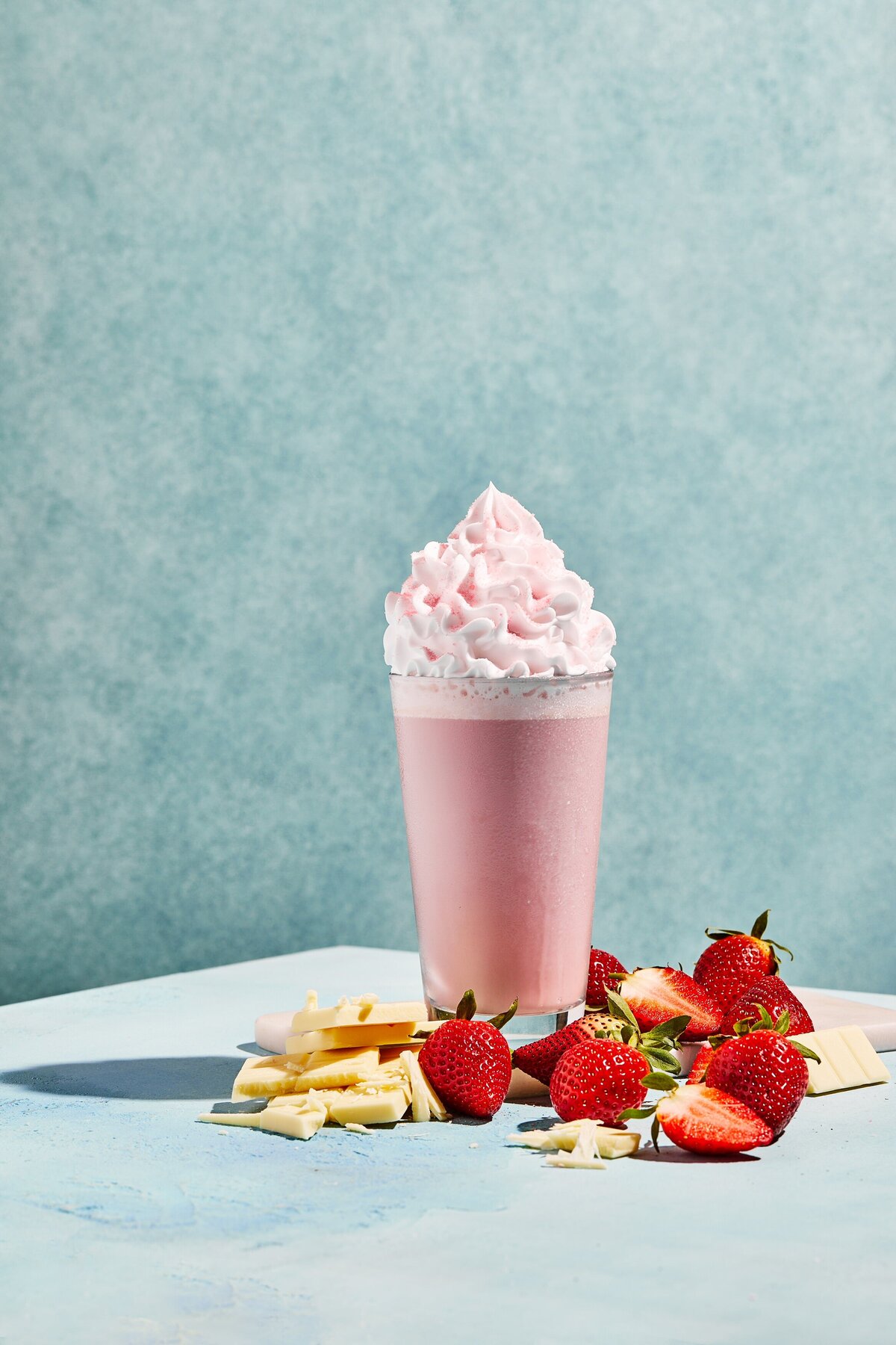 A strawberry milkshake with whipped cream on top and strawberries and bananas in front of it.
