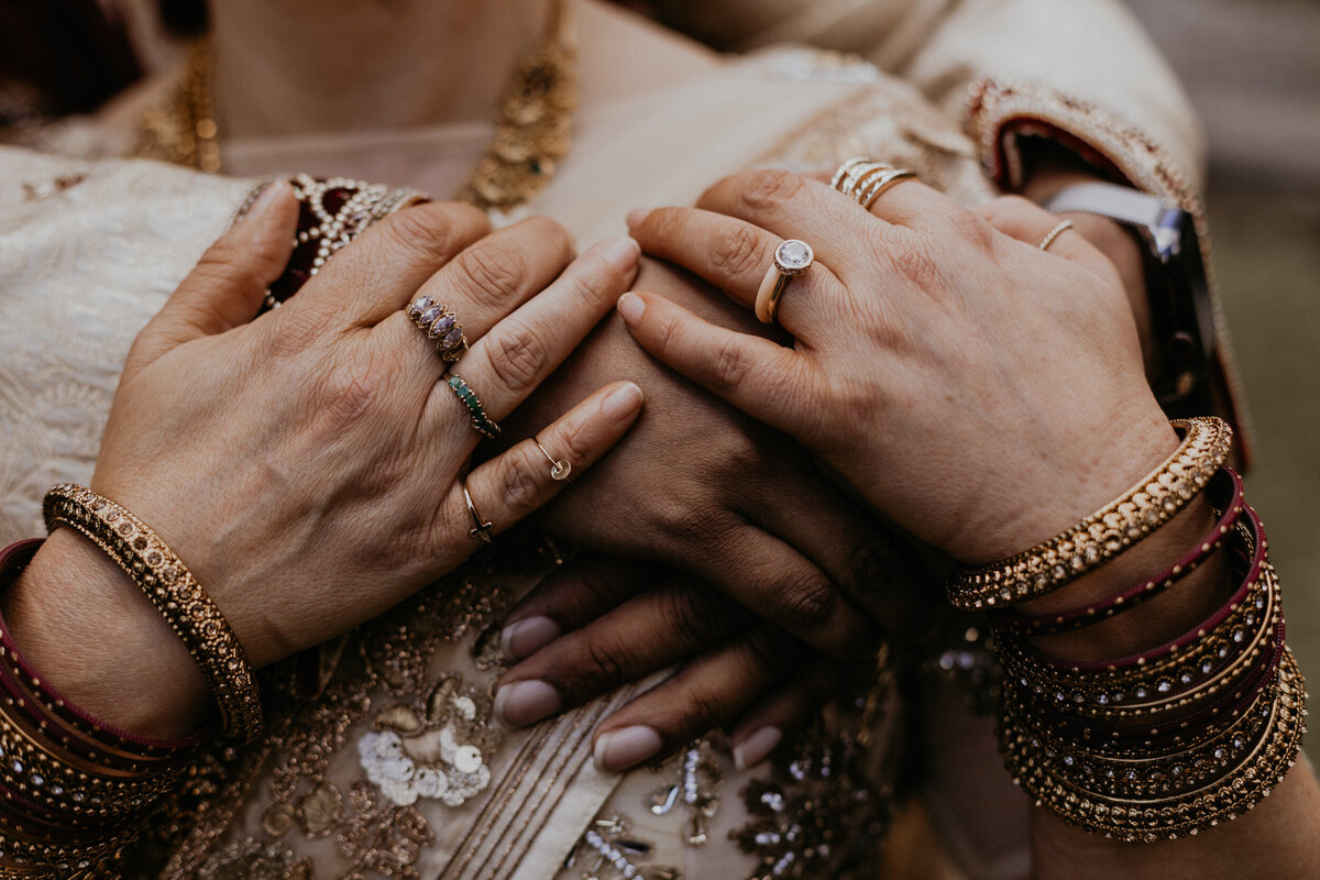 groom holing bride from behind, close up of their hands and jewelry
