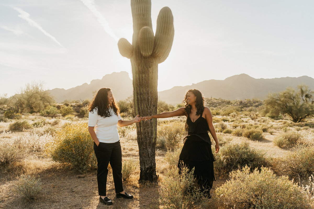 A couple reaching out to hold hands in front of a cactus 