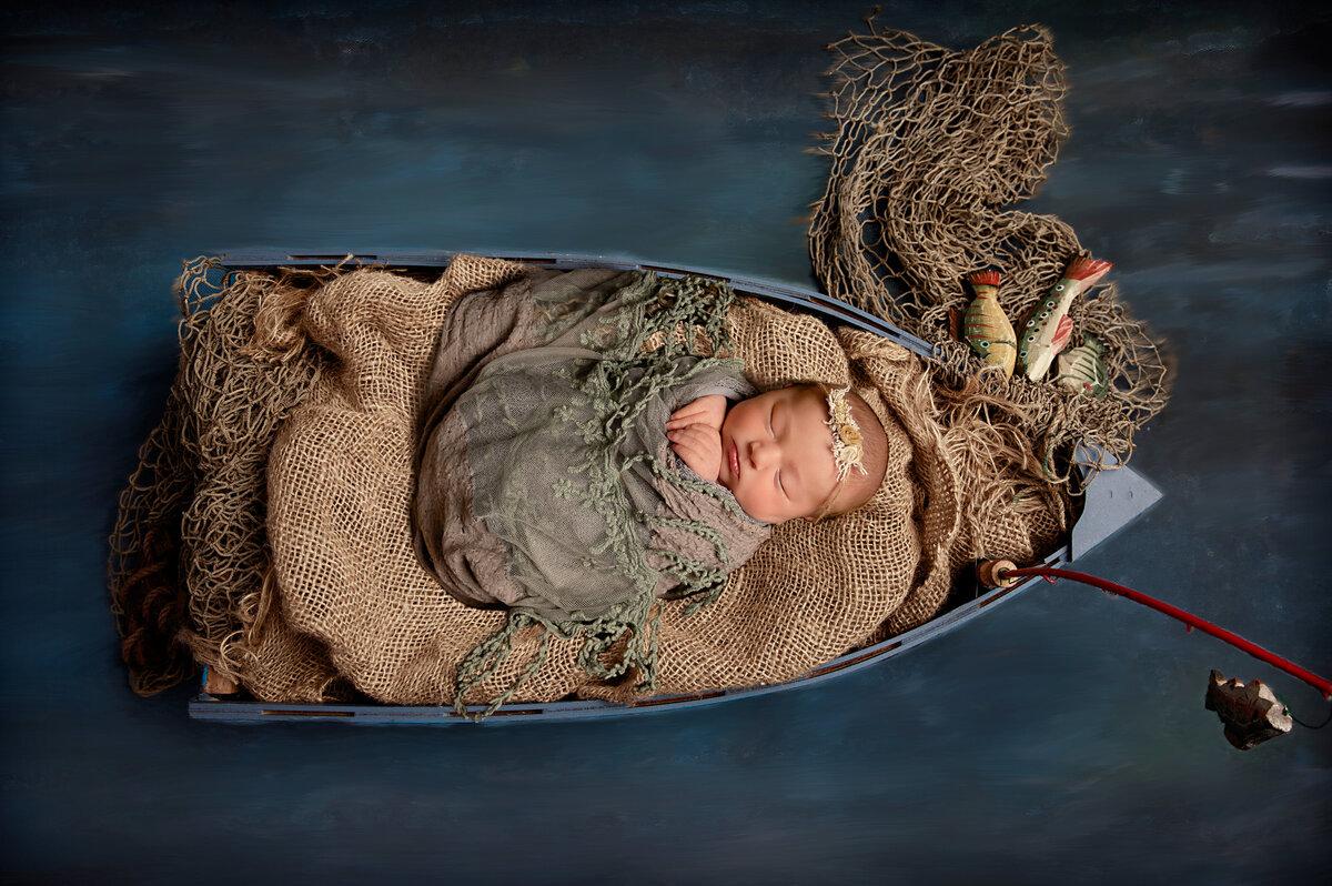 Newborn Girl in Fishing Boat wrapped in a beautiful wrap. Studio located in Quitman, TX. Serving East Texas locations.