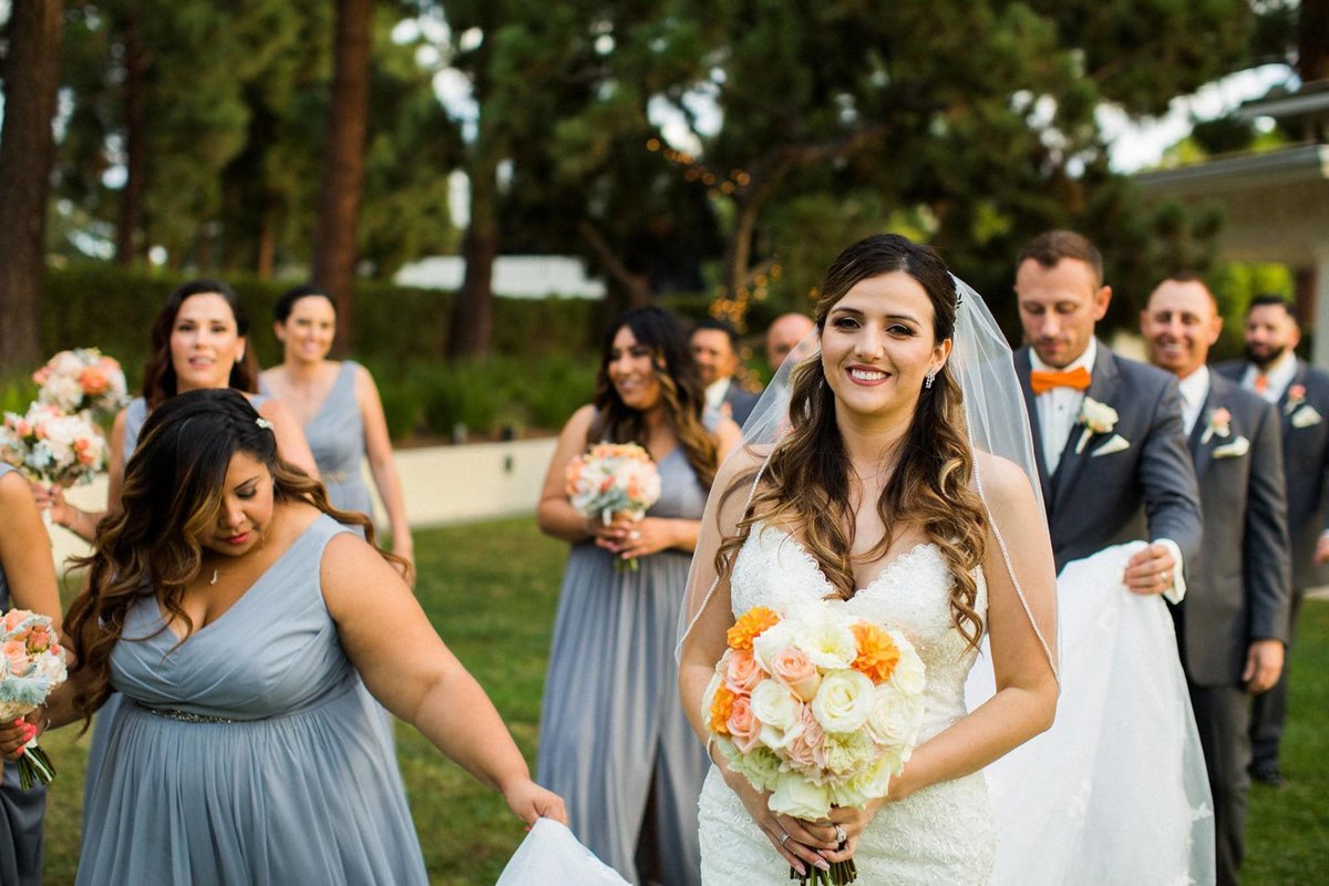 Bridal Party walks towards the camera as Groom holds up Bride's train