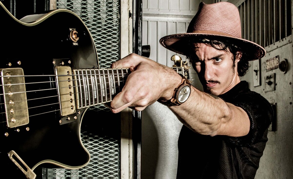 Male musician portrait Taylor John Williams wearing black shirt pink cowboy hat holding outstretched black electric guitar while standing inside old elevator